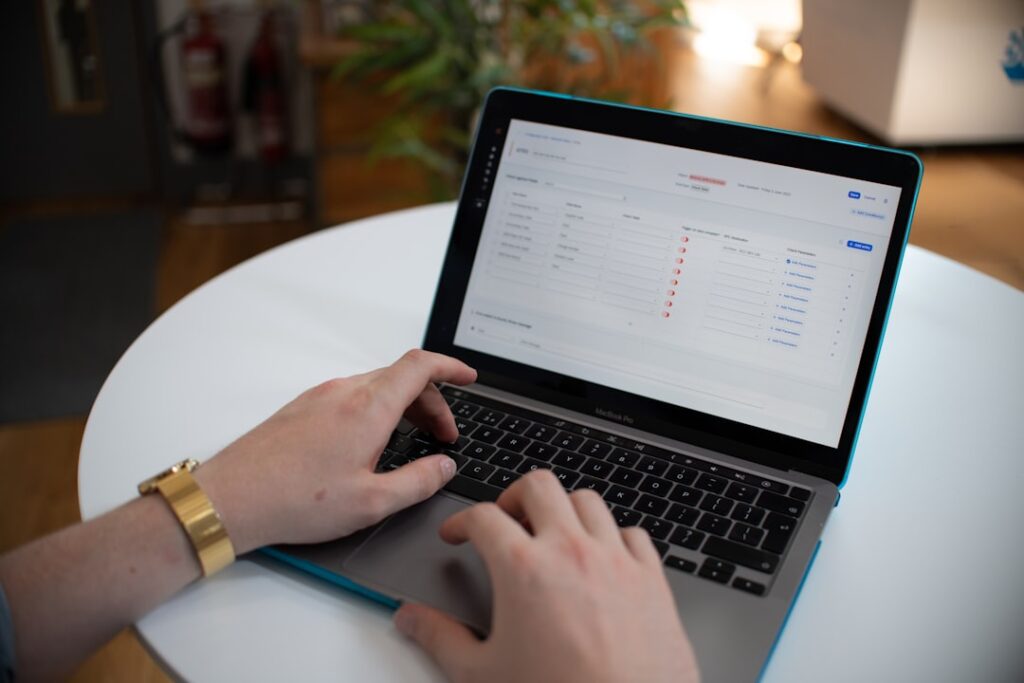 Hands typing on a laptop with a data management spreadsheet on screen