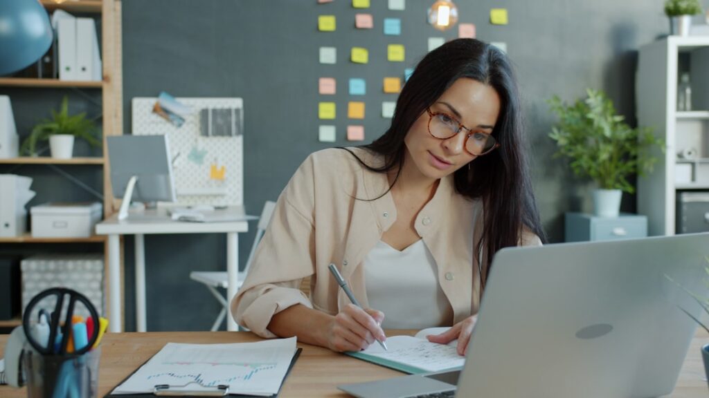Woman working at a desk with laptop and notebook in a modern office