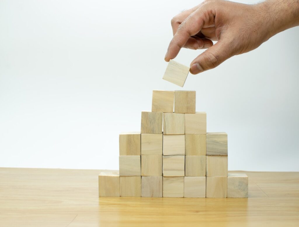 Hand placing wooden block into a pyramid structure representing platform risk