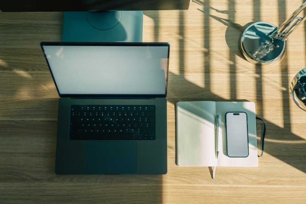 Laptop phone and notebook arranged on a wooden desk workspace